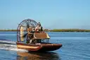 An airboat with a big fan crossing an open lake, trees on the far shore