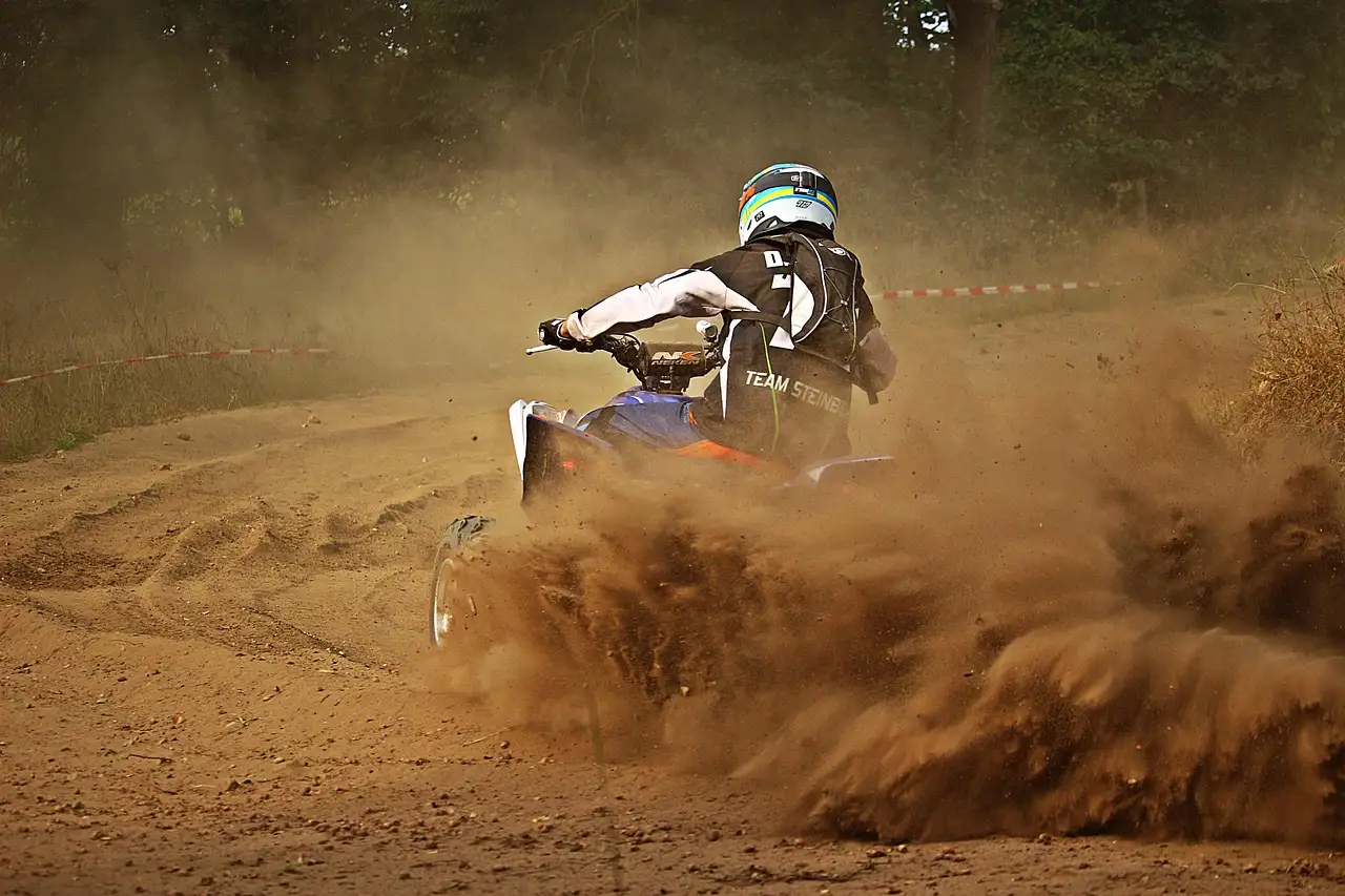 A rider on a quad bike kicking up dust on a sandy track
