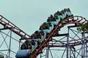 A roller coaster train full of riders climbing a hill of red and white track at a theme park
