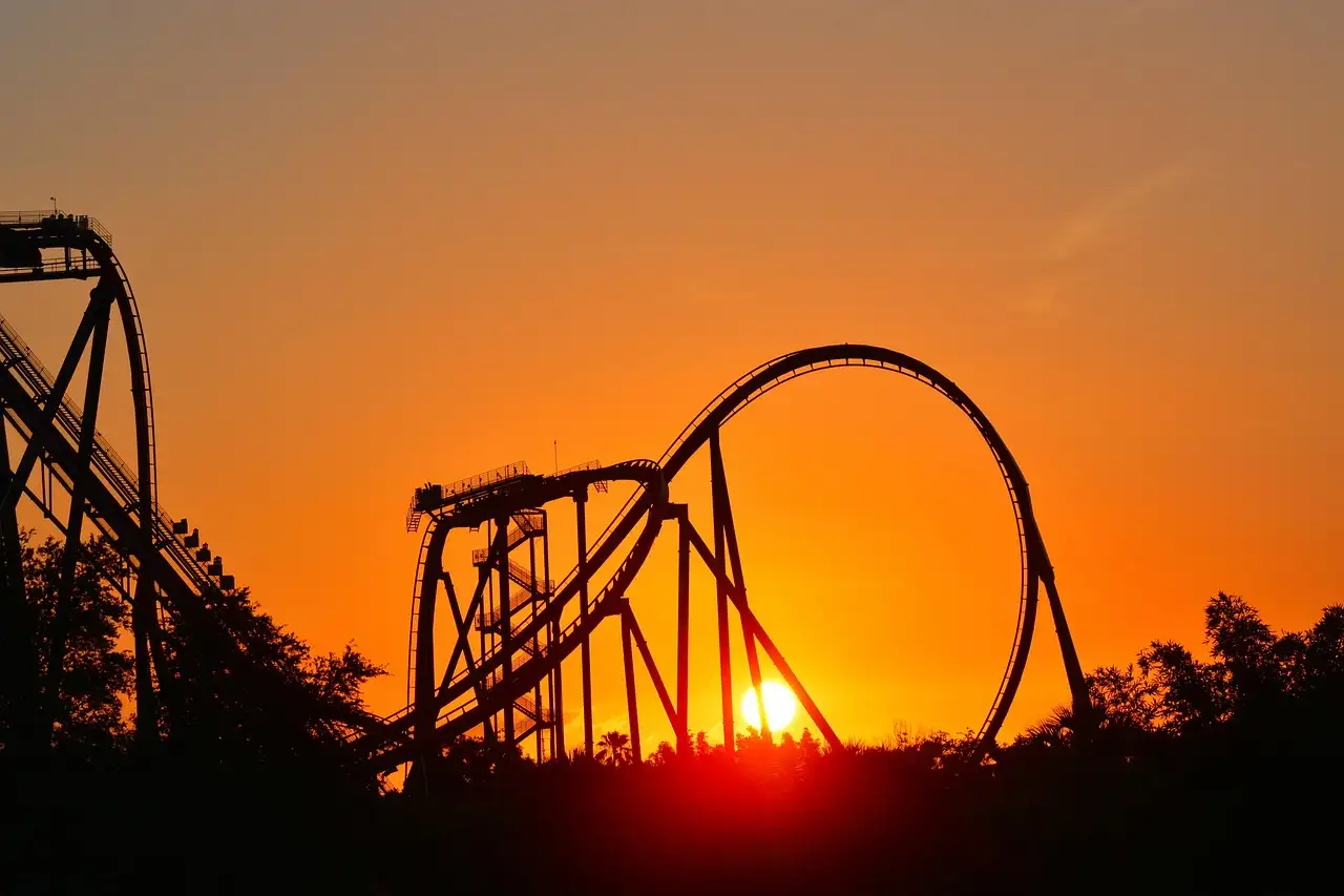 A roller coaster loop in silhouette against an orange sunset