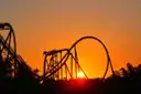 A roller coaster loop in silhouette against an orange sunset