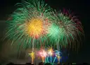 Bright fireworks bursting in green, gold and pink over a city at night