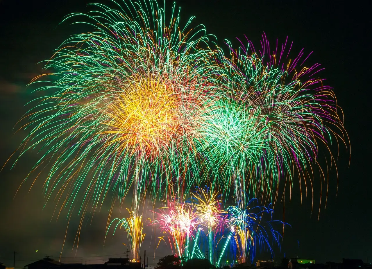 Bright fireworks bursting in green, gold and pink over a city at night