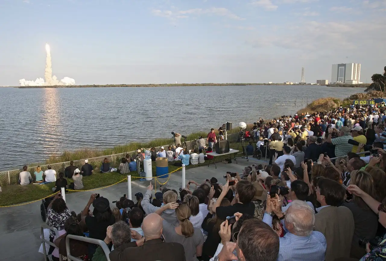 A rocket lifting off from Cape Canaveral across the water as a crowd watches
