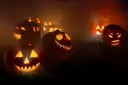 Carved jack-o'-lanterns glowing in thick fog at night
