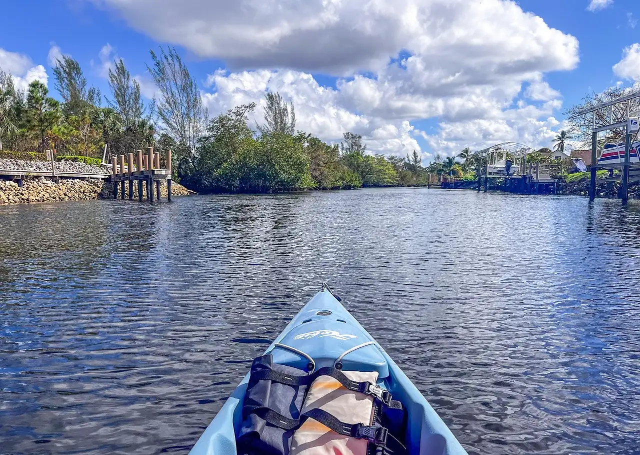 A kayak's bow on open water, with palm trees and a pier ahead