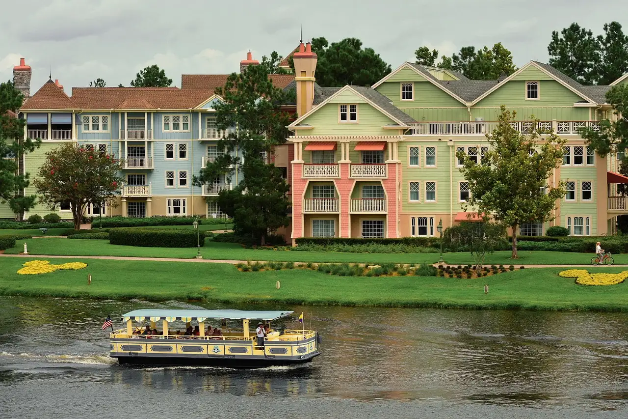 Pastel resort buildings on a lawn by the water near Disney Springs, with a small ferry boat passing