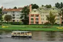 Pastel resort buildings on a lawn by the water near Disney Springs, with a small ferry boat passing