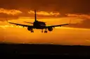 A passenger plane coming in to land against an orange sunset sky