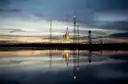 A rocket on its launch tower at sunrise, reflected in calm water