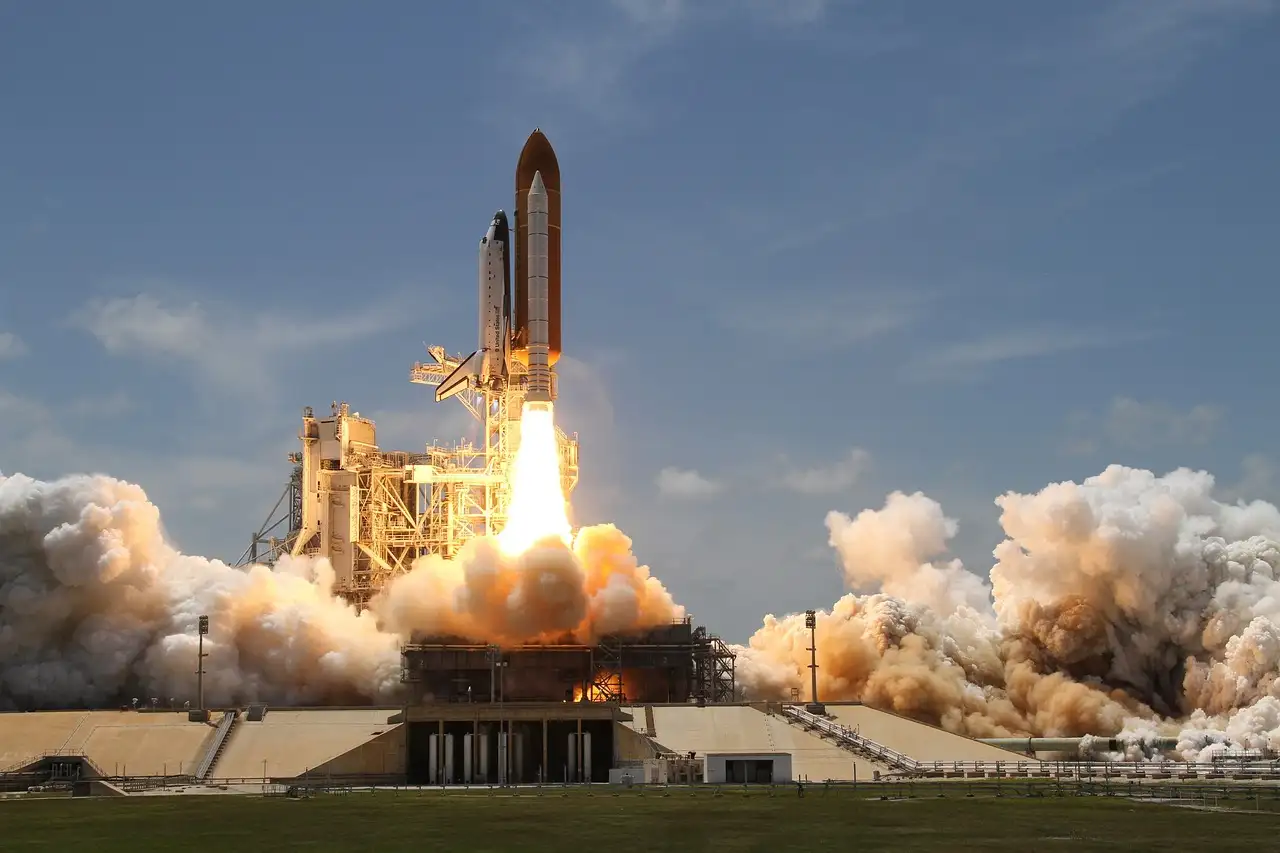 A space shuttle launching by day with white smoke billowing out