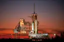 A space shuttle on its launch pad under a red sunset sky