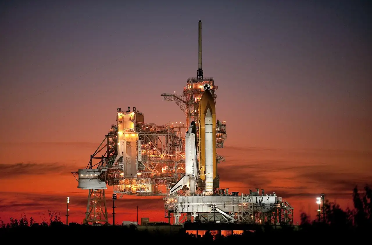 A space shuttle on its launch pad under a red sunset sky