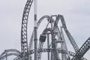 Grey steel roller coaster tracks twisting into loops against a white sky