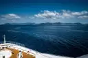 The bow of a cruise ship looking out over blue sea toward a distant coastline