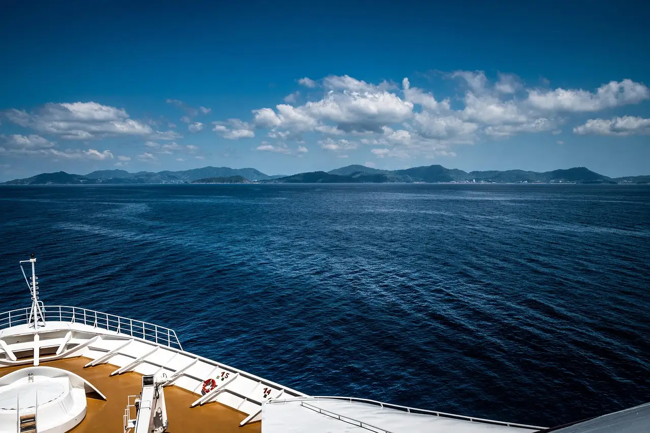 The bow of a cruise ship looking out over blue sea toward a distant coastline