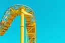 A yellow roller coaster track curving high against a clear blue sky