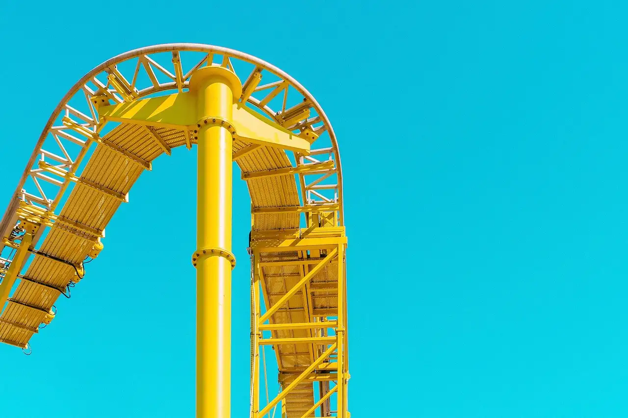 A yellow roller coaster track curving high against a clear blue sky